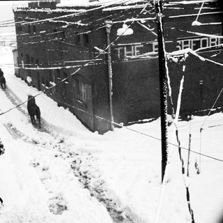Snow-covered city street with people shoveling snow.