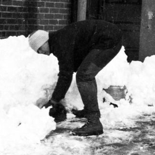Person shoveling heavy snow near brick building.