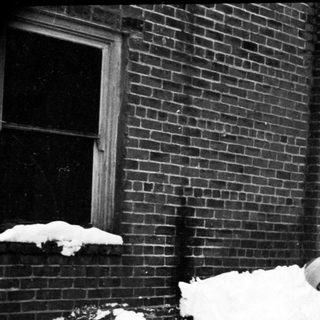 Person shoveling heavy snow near brick building.