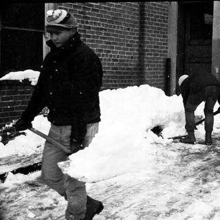 People shoveling snow on a city sidewalk.