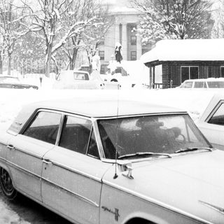 Snow-covered urban street with parked cars.