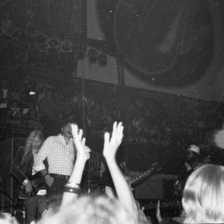 Live band performing on stage with audience raising hands.