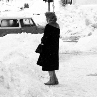Snow-covered street scene with person walking near historic building.