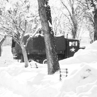 Snow-covered street with parked vintage vehicle.