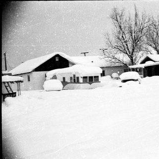 Snow-covered residential area with buried houses and vehicles.