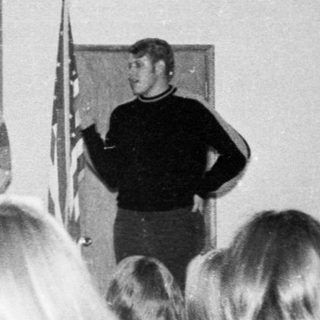 People attending indoor presentation with speakers and audience.
