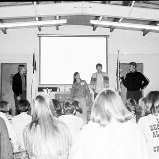 People attending indoor presentation with speakers and audience.