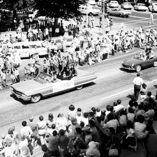Large crowd cheering during a parade with open convertible cars.