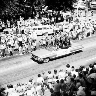Large crowd cheering during a parade with open convertible cars.