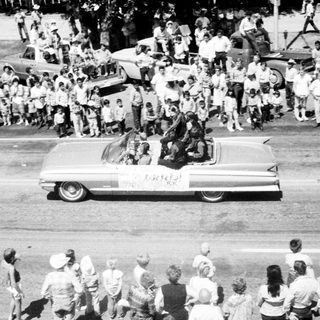 Classic car parade with crowd cheering.