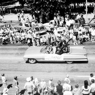 Classic car parade with crowd cheering.
