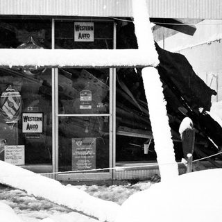 Snow-covered storefront with broken glass and damage.