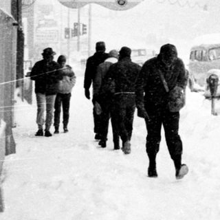 Snowy street scene with pedestrians walking near Curiosity Corner and McDonald Realty signs.