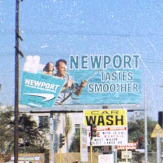 Vintage street scene with classic car, Newport billboard, 1960s-70s era.