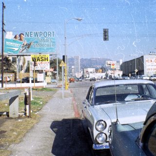 Vintage street scene with classic car, Newport billboard, 1960s-70s era.