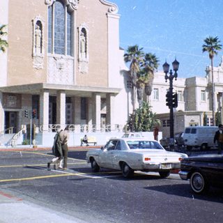 Vintage street scene with historic building, palm trees, and 1970s vehicles.