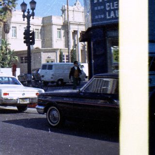 Vintage street scene with historic building, palm trees, and 1970s vehicles.
