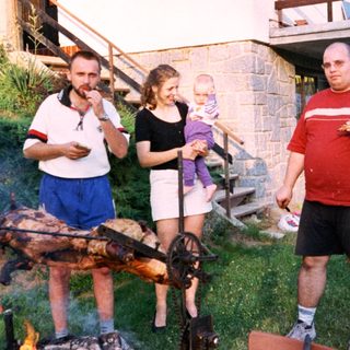 People barbecuing outdoors with children in backyard.