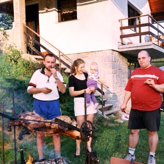 People barbecuing outdoors with children in backyard.