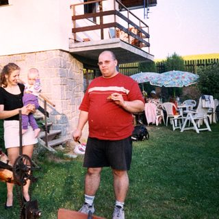 People barbecuing outdoors with children in backyard.