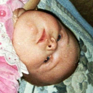 Baby wearing pink onesie, held by adult.