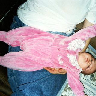 Baby wearing pink onesie, held by adult.