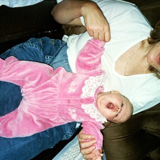 A woman holds a baby in a pink outfit.