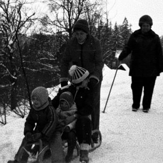 Family skiing on snowy trail with child in sled.