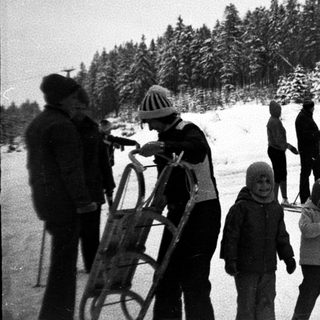 Family skiing and sledding in snowy forest.