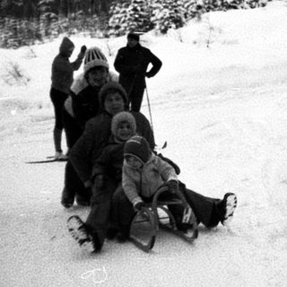 People sledding down snowy hill in forested area.
