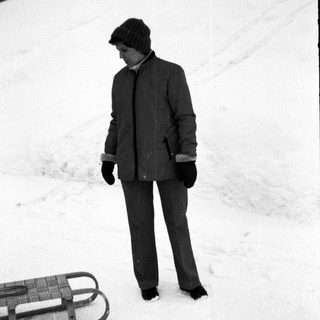 Person in winter clothing standing on snow near sled.
