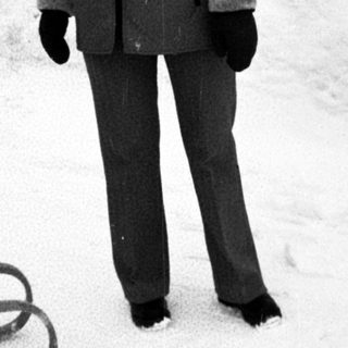 Person in winter clothing standing on snow near sled.
