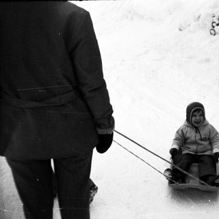 Child sledding downhill with adult holding reins.