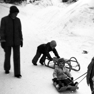 Children sledding down snowy hill with adult supervision.
