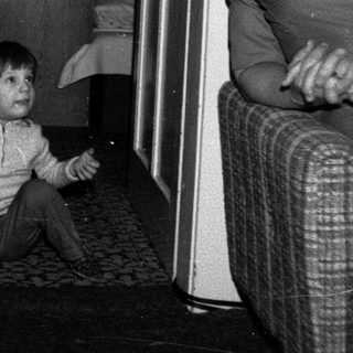 Child sitting on floor with suitcase, adult standing nearby.