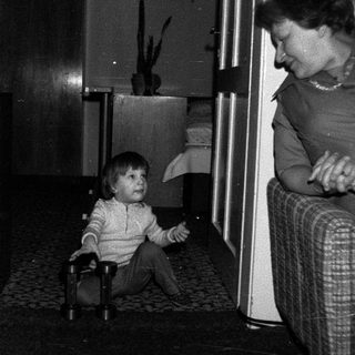 Child sitting on floor with suitcase, adult standing nearby.