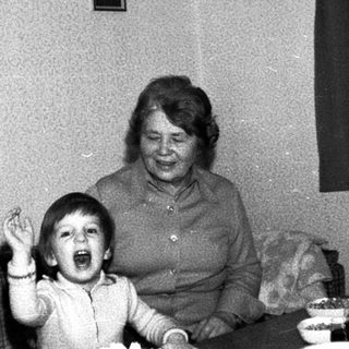 Family gathering with elderly couple and child laughing indoors.