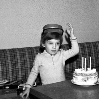Child wearing hat blows out birthday cake candles.
