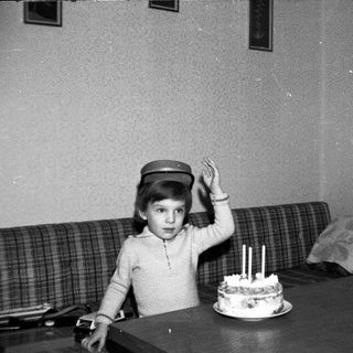 Child wearing hat blows out birthday cake candles.
