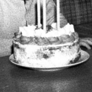 Child sitting at table with birthday cake and lit candles.