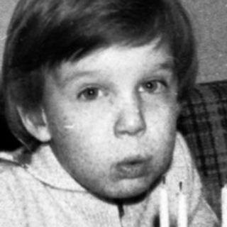 Child sitting at table with birthday cake and lit candles.