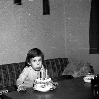 Child sitting at table with birthday cake and lit candles.