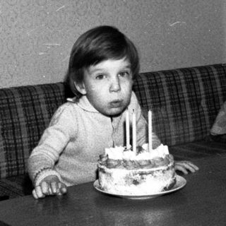 Child sitting at table with birthday cake and lit candles.