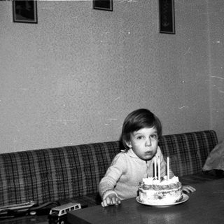 Child sitting at table with birthday cake and lit candles.