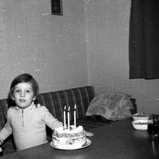 Child sitting by cake with lit candles.