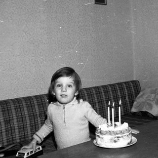 Child sitting by cake with lit candles.