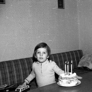 Child sitting by cake with lit candles.