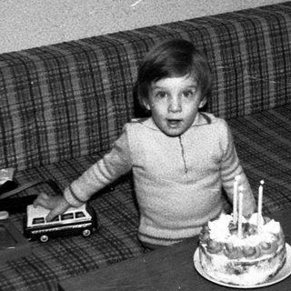 Young child surprised by birthday cake with lit candles.
