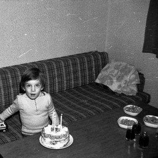 Young child surprised by birthday cake with lit candles.