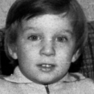 Young child sitting with birthday cake and lit candles.